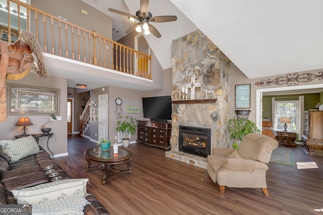 living room featuring dark wood-type flooring, ceiling fan, a stone fireplace, and high vaulted ceiling