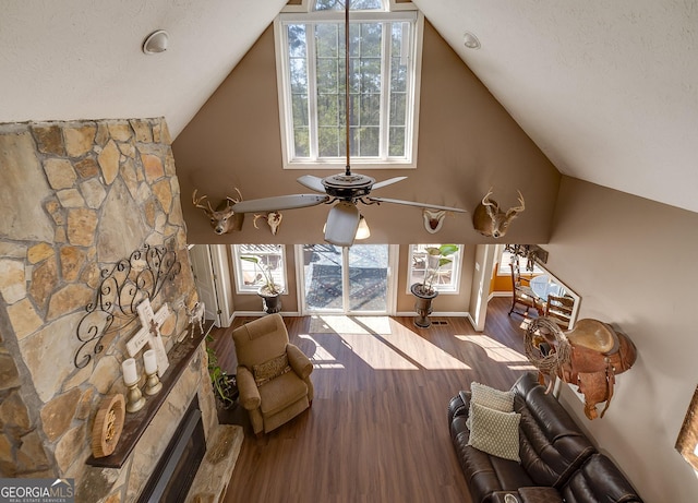 living room featuring a stone fireplace, vaulted ceiling, a textured ceiling, hardwood / wood-style flooring, and ceiling fan