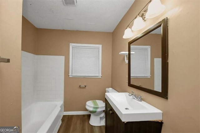 bathroom featuring a bathing tub, vanity, wood-type flooring, a textured ceiling, and toilet