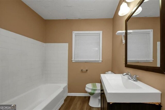 bathroom with a bathing tub, sink, hardwood / wood-style floors, and toilet