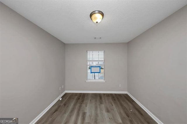 spare room featuring dark wood-type flooring and a textured ceiling