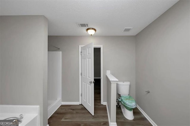 bathroom with a textured ceiling, wood-type flooring, plus walk in shower, and toilet