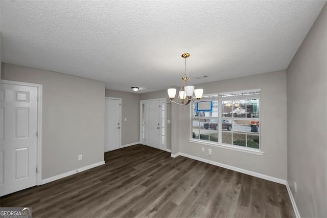 unfurnished dining area with dark hardwood / wood-style flooring, a textured ceiling, and a chandelier