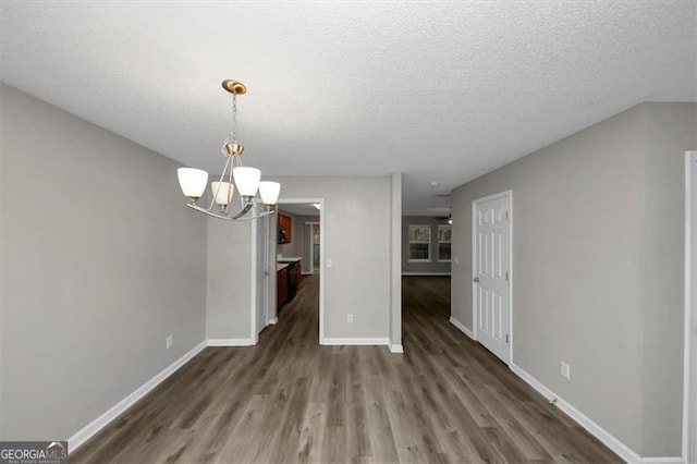 unfurnished dining area with dark hardwood / wood-style floors, an inviting chandelier, and a textured ceiling