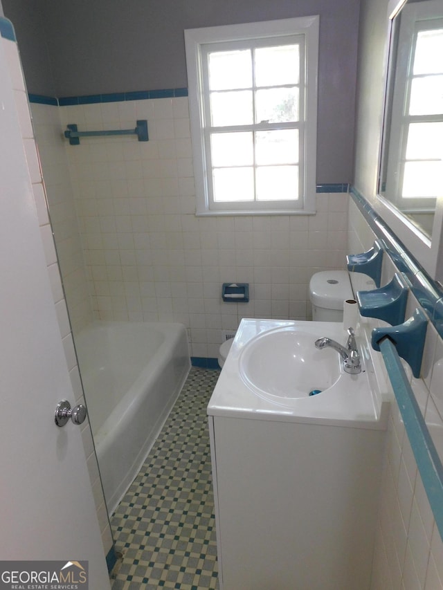 bathroom with toilet, a bathing tub, tile walls, and a wealth of natural light