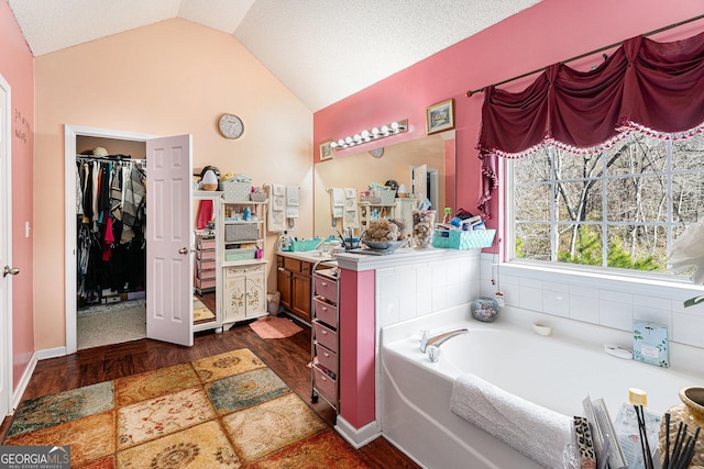 bathroom featuring a bathing tub, vanity, vaulted ceiling, and hardwood / wood-style floors