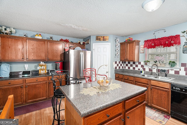 kitchen featuring sink, light wood-type flooring, stainless steel refrigerator, dishwasher, and a kitchen island