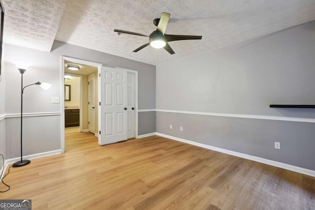 empty room with ceiling fan, a textured ceiling, and light wood-type flooring