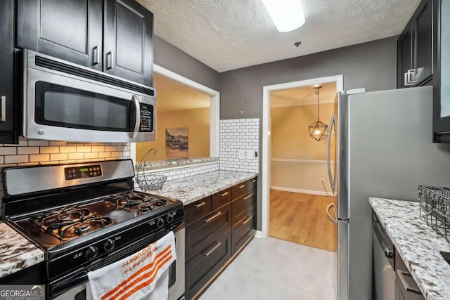 kitchen featuring light stone counters, appliances with stainless steel finishes, hanging light fixtures, and backsplash