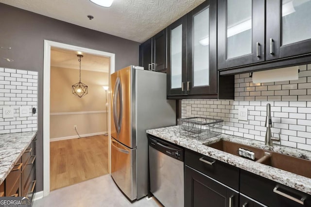 kitchen with sink, hanging light fixtures, stainless steel appliances, light stone counters, and decorative backsplash