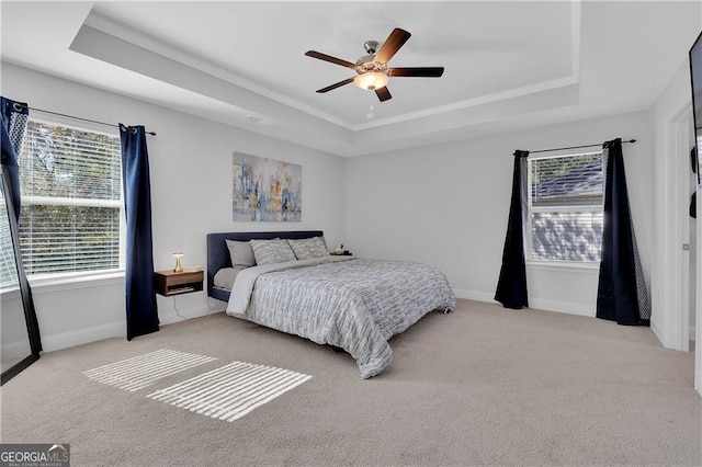 bedroom with light colored carpet, ceiling fan, and a tray ceiling