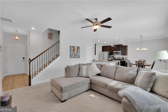 living room featuring light carpet, ceiling fan with notable chandelier, and crown molding