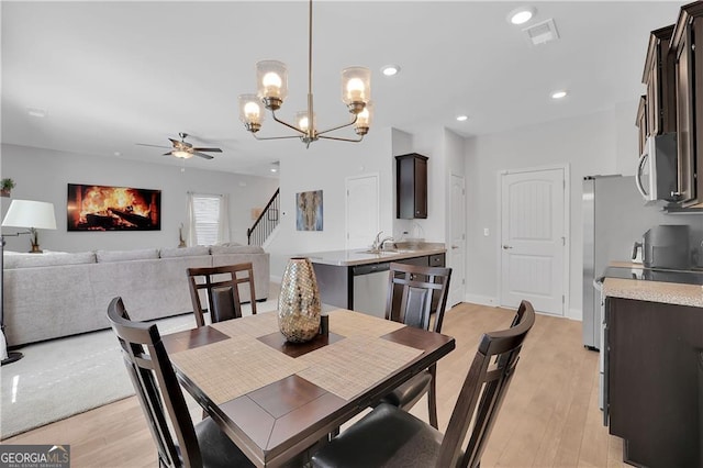 dining space with sink, ceiling fan with notable chandelier, and light hardwood / wood-style flooring