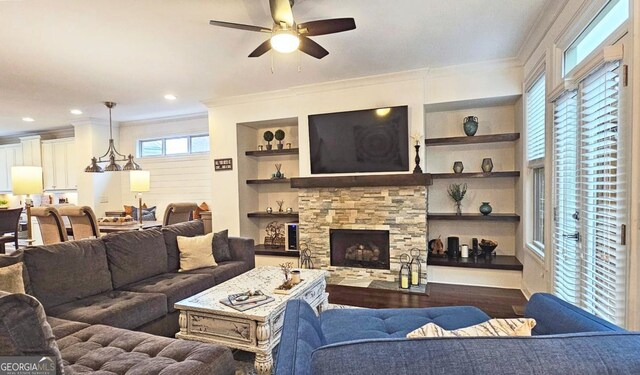 living room featuring dark hardwood / wood-style flooring, ceiling fan, a stone fireplace, and a healthy amount of sunlight