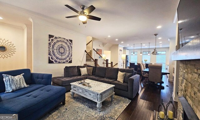 living room with ornamental molding, a stone fireplace, dark wood-type flooring, and ceiling fan