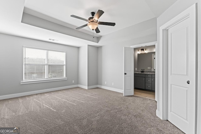 unfurnished bedroom featuring light carpet, a tray ceiling, ensuite bath, and ceiling fan