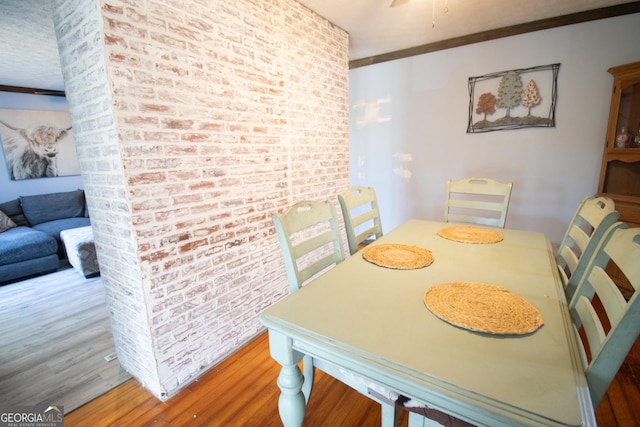 dining area with hardwood / wood-style floors and brick wall