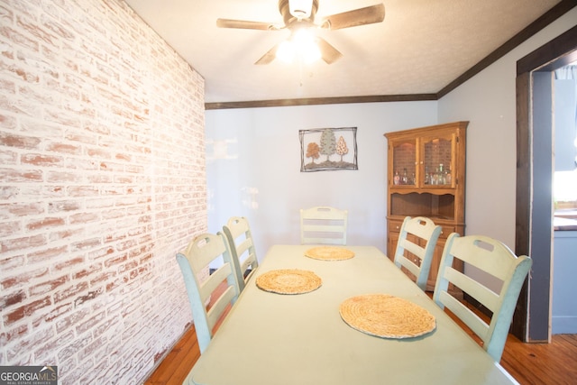 dining space with hardwood / wood-style flooring, crown molding, brick wall, and ceiling fan