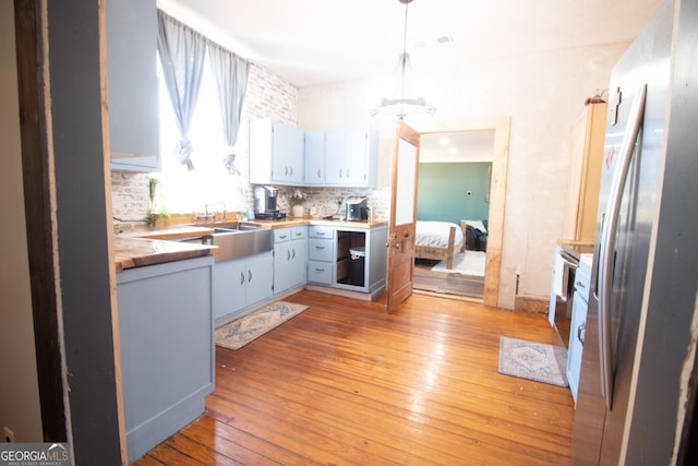 kitchen with stainless steel refrigerator, decorative light fixtures, sink, decorative backsplash, and light wood-type flooring