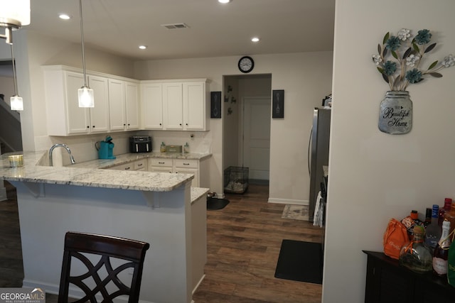 kitchen featuring a kitchen bar, hanging light fixtures, stainless steel refrigerator, kitchen peninsula, and white cabinets