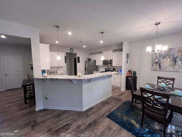 kitchen with dark wood-type flooring, decorative light fixtures, appliances with stainless steel finishes, kitchen peninsula, and white cabinets