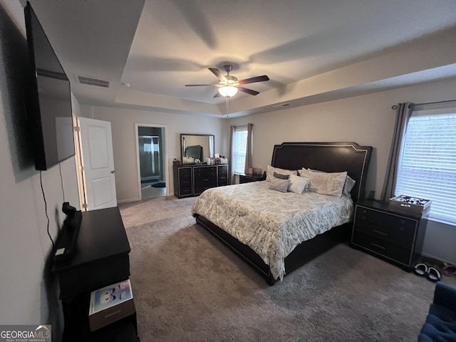 carpeted bedroom featuring ceiling fan, a raised ceiling, and multiple windows