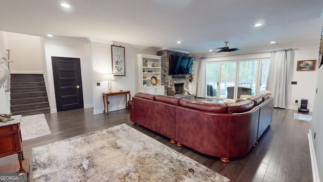 living room with ornamental molding, a stone fireplace, ceiling fan, and dark hardwood / wood-style flooring