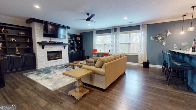 living room featuring ceiling fan, a fireplace, ornamental molding, a textured ceiling, and dark hardwood / wood-style flooring