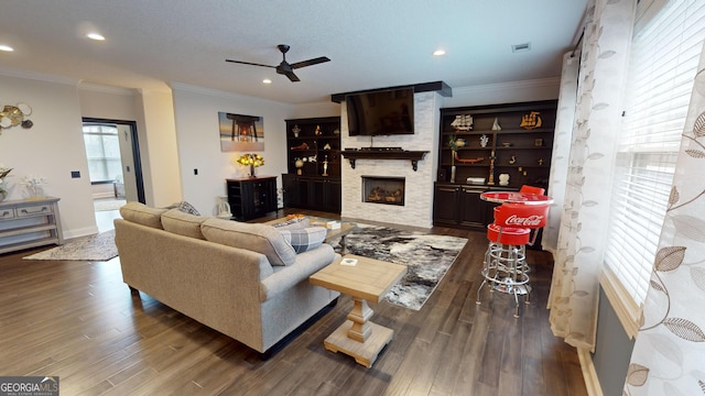 living room featuring ceiling fan, ornamental molding, wood-type flooring, and a fireplace