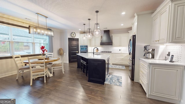 kitchen featuring custom exhaust hood, white cabinetry, a kitchen island with sink, and pendant lighting