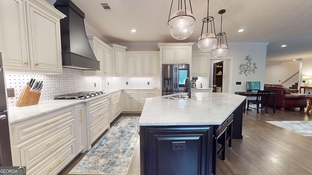 kitchen with sink, custom exhaust hood, decorative light fixtures, stainless steel appliances, and a kitchen island with sink