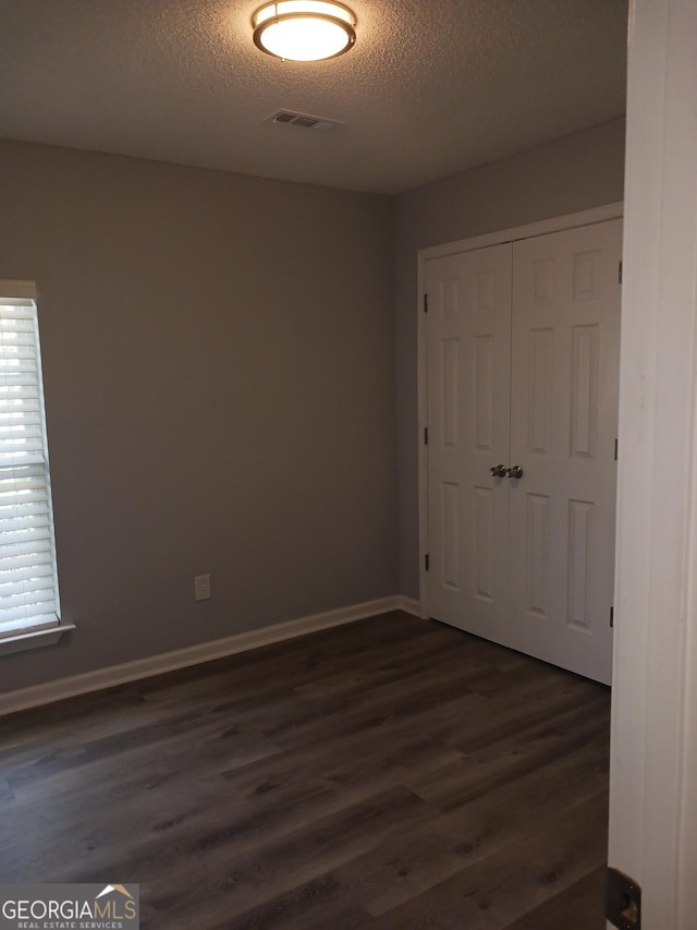 unfurnished bedroom featuring dark hardwood / wood-style floors, a textured ceiling, and a closet