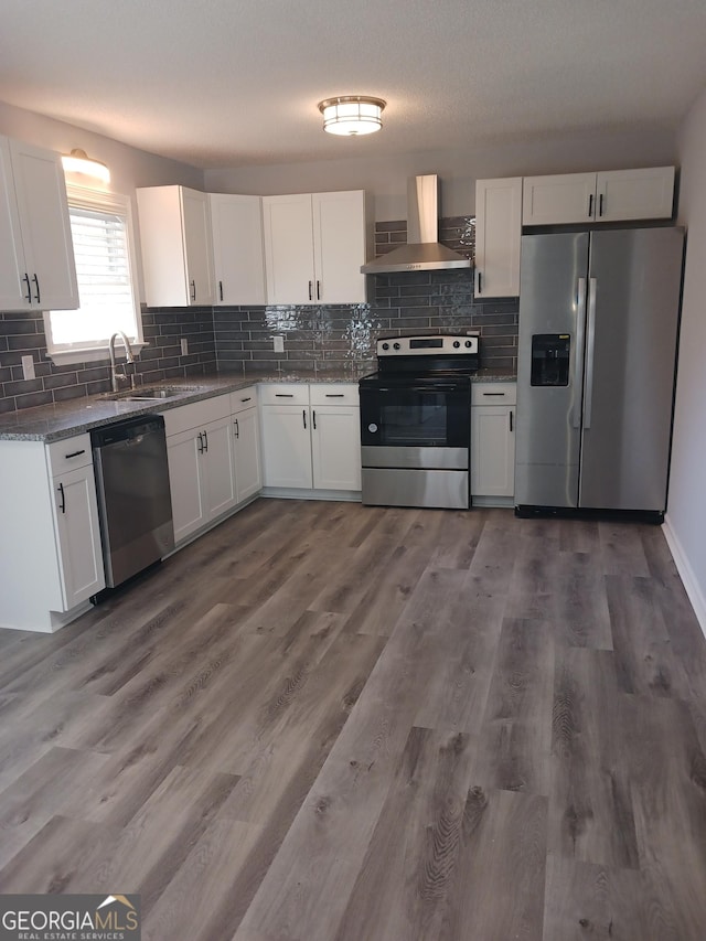 kitchen featuring wall chimney exhaust hood, sink, light stone counters, appliances with stainless steel finishes, and white cabinets