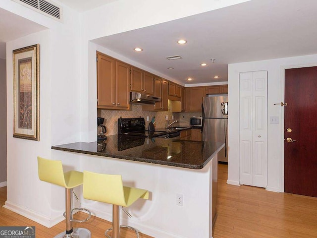 kitchen with appliances with stainless steel finishes, dark stone countertops, a kitchen breakfast bar, and kitchen peninsula