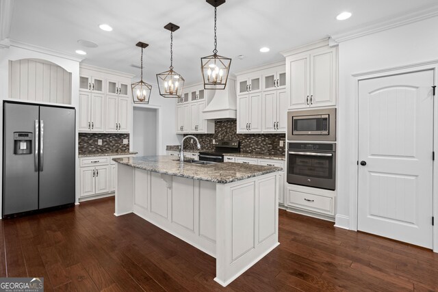 kitchen featuring premium range hood, an island with sink, appliances with stainless steel finishes, white cabinetry, and a sink