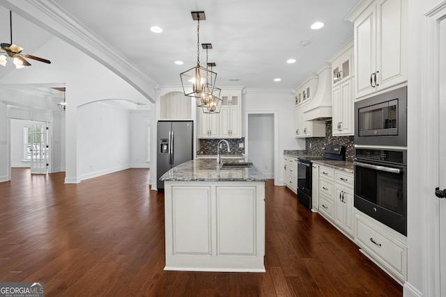 kitchen featuring custom exhaust hood, arched walkways, a sink, appliances with stainless steel finishes, and open floor plan