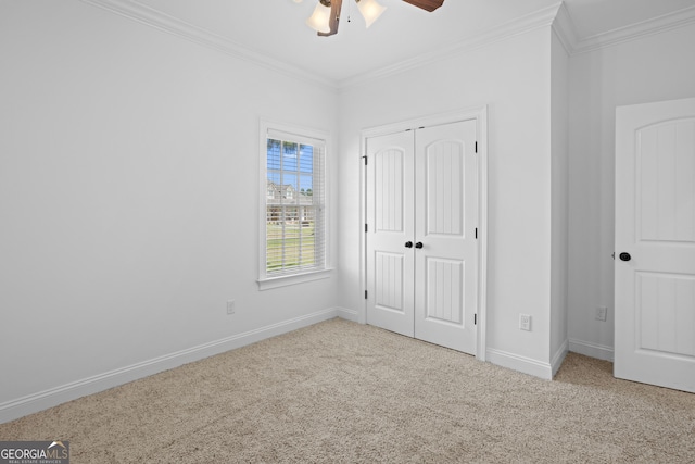 unfurnished bedroom with crown molding, baseboards, carpet, a closet, and a ceiling fan