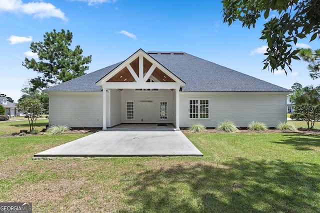 back of property featuring a lawn, roof with shingles, and a patio area