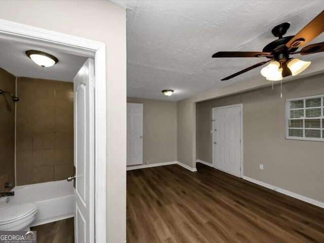 interior space featuring tiled shower / bath, wood-type flooring, toilet, and a textured ceiling