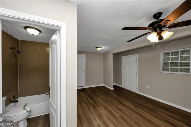 interior space with tiled shower / bath, hardwood / wood-style flooring, ceiling fan, toilet, and a textured ceiling