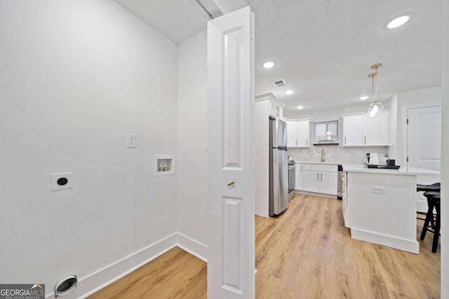 kitchen featuring pendant lighting, stainless steel refrigerator, white cabinetry, backsplash, and a kitchen breakfast bar