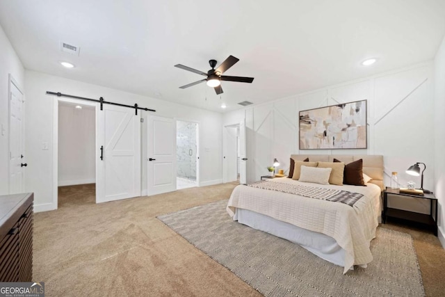 carpeted bedroom featuring ensuite bathroom, a barn door, and ceiling fan