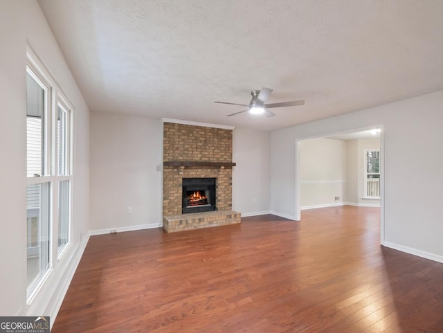 unfurnished living room featuring dark wood-type flooring, ceiling fan, a fireplace, and a textured ceiling