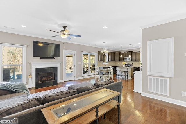 living area with dark wood-style floors, crown molding, visible vents, a fireplace with flush hearth, and baseboards