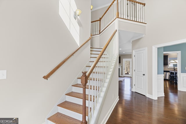 staircase with ornamental molding, a towering ceiling, and hardwood / wood-style floors