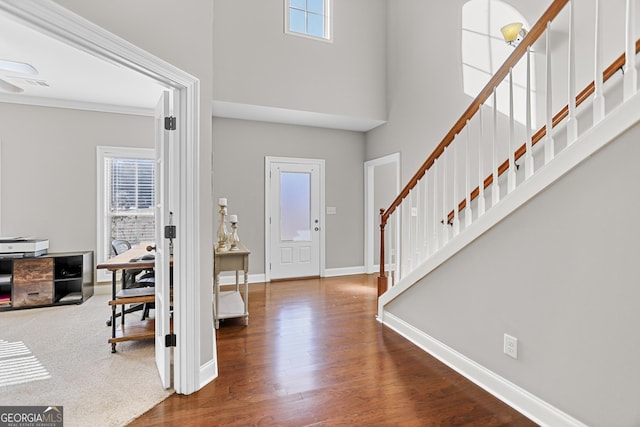 foyer with wood finished floors, a towering ceiling, baseboards, stairway, and crown molding