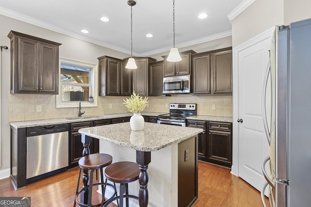 kitchen with dark brown cabinetry, appliances with stainless steel finishes, wood finished floors, a center island, and a sink