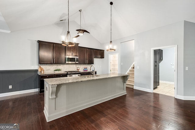 kitchen with stainless steel microwave, stove, a sink, dark brown cabinets, and light stone countertops