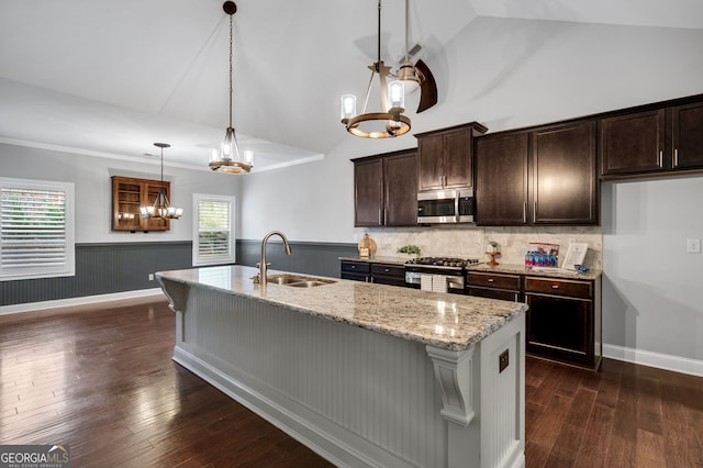 kitchen featuring a wainscoted wall, stainless steel appliances, a sink, light stone countertops, and dark wood finished floors