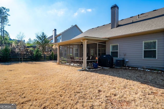 rear view of property featuring a shingled roof, a sunroom, a chimney, fence, and a yard